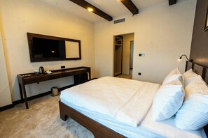 A bedroom with a bed, a desk, a mirror, and a door leading to a bathroom.