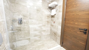 Una ducha con puerta de vidrio, una puerta de madera y un perchero con una toalla.