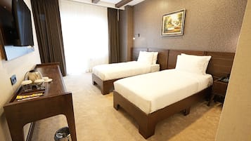 Habitación de hotel con dos camas, un escritorio con cafetera, un cesto de basura y un cuadro en la pared.