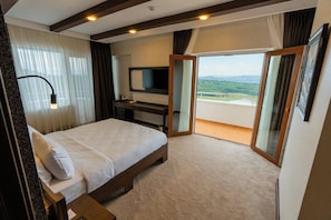 A bedroom with a bed, a desk, a TV, and a balcony with a view.