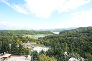 Vista de um vale arborizado com um lago e colinas ao longe.