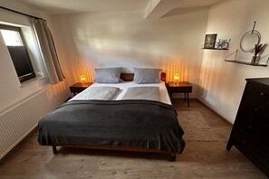 A bedroom with a bed, bedside lamps, a window with curtains, a radiator, and a dresser. - House Hölzene "Ilke" (Gersfeld)