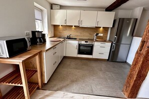A compact kitchen with white cabinets, a stainless steel refrigerator, a microwave, and a coffee maker. - House Hölzene "Ilke" (Gersfeld)