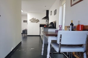 Eine moderne Küche mit Essbereich, inklusive eines weißen Stuhls, einem Holztisch und einer Kaffeemaschine.