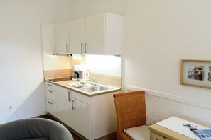 A compact kitchenette with a sink, a coffee maker, and a wicker chair. - Holiday apartment with 1 bedroom (Borkum)