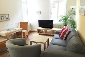 A living room with a sofa, a television on a stand, a small table, and a chair. - Holiday apartment with 1 bedroom (Borkum)