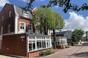 A two-story residential building with a brick facade, a conservatory, and a tree in front. - Holiday apartment with 1 bedroom (Borkum)