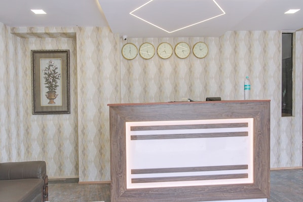 Un área de recepción con un mostrador de madera, una obra de arte floral enmarco y una fila de relojes de pared.