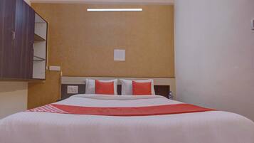 A hotel room with a bed, a nightstand, a mirror, and a wall-mounted light fixture.