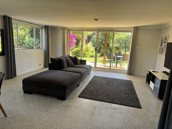 A modern living room with a sectional sofa, a flat-screen TV, and a sliding glass door leading to a patio area.