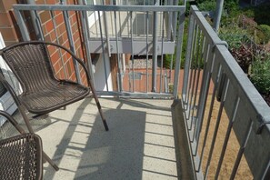 A balcony with a metal railing, a wicker chair, and a view of a building with a brick facade. - 18 in the Stranddüne house (Haffkrug)