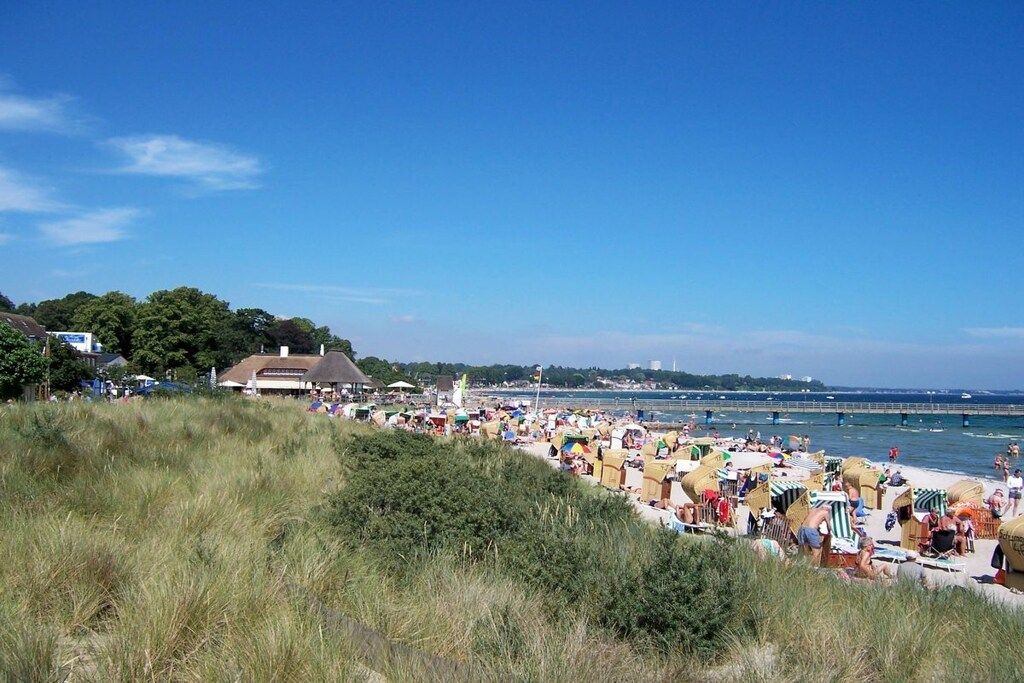 Ein Strand mit Menschen, Sonnenschirmen und einem Gebäude im Hintergrund.