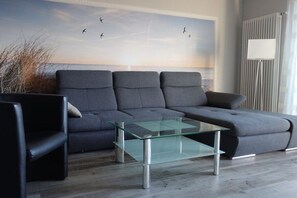 Een moderne woonkamer met een hoekbank, een glazen salontafel en een muurschildering.