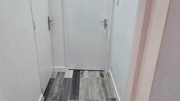 A narrow hallway with a door at the end, tiled flooring, and a white wall.