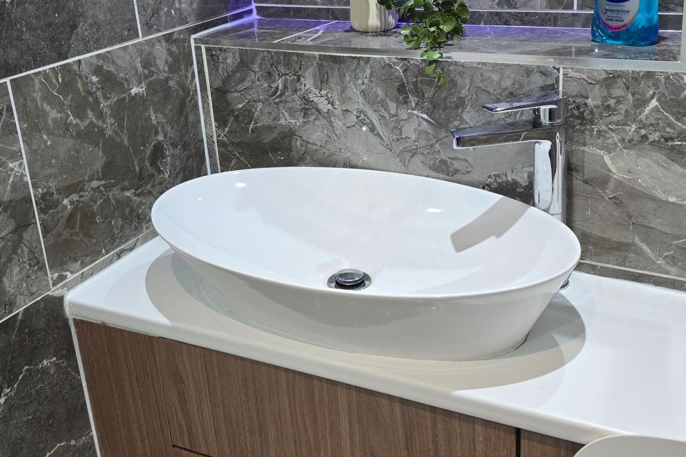 A bathroom with a white vessel sink, a wooden cabinet below, and a marble backsplash.