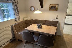 A corner dining area with a wooden table, two chairs, a flower vase, a clock, and a radiator. - Holiday home with 1 bedroom (Kirchlinteln)