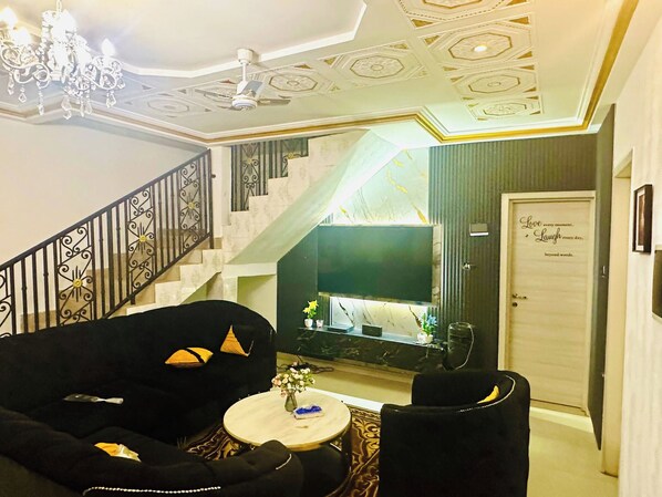 Una sala de estar con escalera, un candelabro y un televisor de pantalla plana.