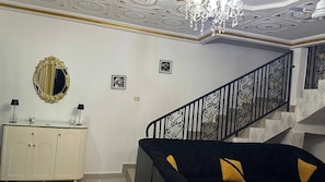 A room with a staircase, a chandelier, a mirror, and a sofa.