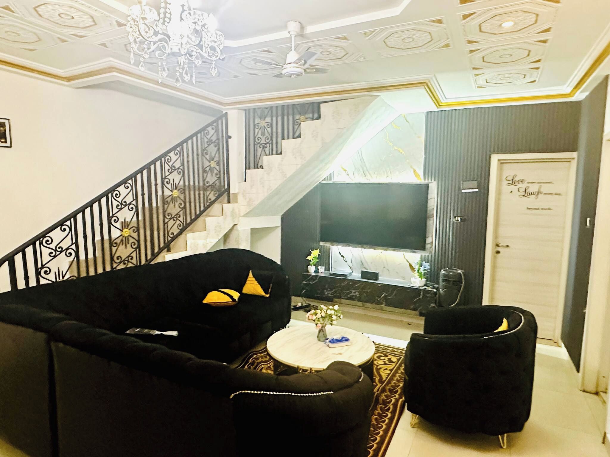 Un salon avec un escalier, un lustre et une porte sur laquelle est apposée une plaque.