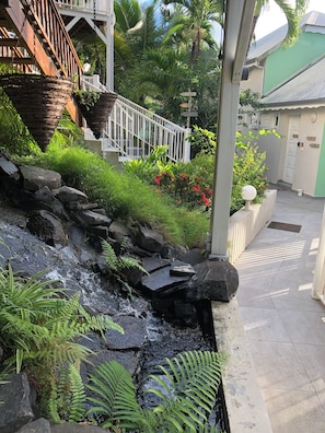 A stone water feature with ferns, a white staircase, and a green wall with a door. - Tropikal Cottage. Sea view in Deshaies. Swimming pool. (Deshaies)