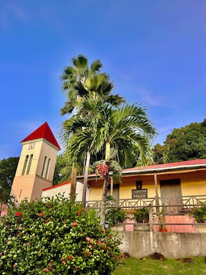 A building with a clock tower, a sign reading 'Honeymoon Police,' and a palm tree with red flowers. - Tropikal Cottage. Sea view in Deshaies. Swimming pool. (Deshaies)