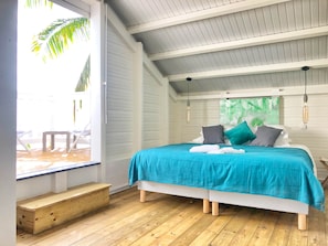 A bedroom with a bed, wooden floor, and a view of the outdoors. - Villa O Coeur de Deshaies. Sea view. Swimming pool (Deshaies)