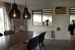 Ein Essbereich mit Holztisch und Stühlen, Pendelleuchten, einem Fenster mit Blick und einem Weinkühlschrank mit Flaschen und Gläsern.
