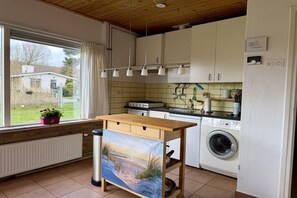 Een keuken met uitzicht op een huis, een wasmachine en een tafel met een schilderij.