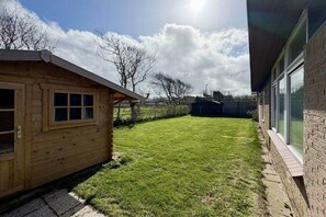 A wooden cabin with a fenced yard, a brick building, and a clear sky. - Holiday home with 2 bedrooms (Julianadorp)