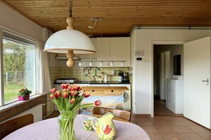 A kitchen with a wooden ceiling, a dining table with a vase of tulips, and a view of the outdoors. - Holiday home with 2 bedrooms (Julianadorp)