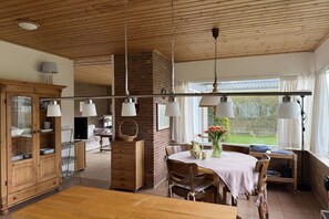A spacious kitchen with wooden cabinets, a dining table, and hanging pendant lights. - Holiday home with 2 bedrooms (Julianadorp)