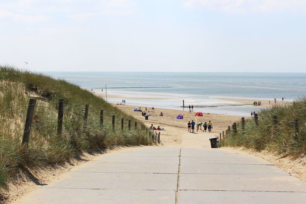 Un sendero bordeando la playa que lleva a la orilla, con gente y tiendas de campaña.