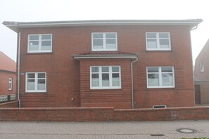 A two-story brick building with multiple windows, a flat roof, and a paved ground. - Short break Borkum 2 (Borkum)
