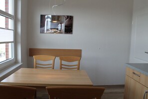 A dining area with a wooden table and chairs, a hanging light fixture, and a framed picture on the wall. - Short break Borkum 2 (Borkum)
