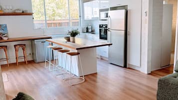 Une cuisine moderne avec des meubles blancs, un réfrigérateur en acier inoxydable et un coin bar avec des tabourets.
