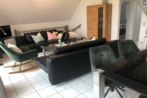 Un salon moderne avec un canapé noir, un fauteuil vert et une table à manger avec des chaises.