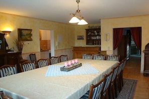 A dining room with a long table set for six, surrounded by chairs. There is a chandelier above the table, and a bar area with bottles and glasses is visible in the background. - Castle in Buttlar with swimming pool (Buttlar)