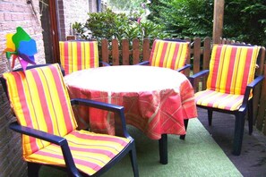 A round table with six chairs, each with striped cushions, set on a green mat. - Holiday home in Borkum with swimming pool (Borkum)