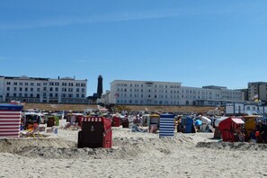 A beach with beach huts and a large building in the background. - Holiday apartment with 4 bedrooms (Borkum)