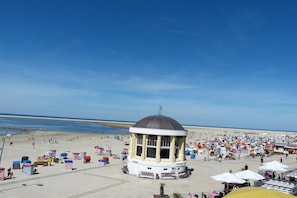 Een strand met een tuinhuisachtige constructie, parasols en mensen op het strand.