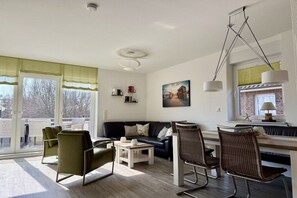 A modern living room with a sofa, chairs, a coffee table, and a dining area with a table and chairs. - Holiday apartment with 4 bedrooms (Borkum)
