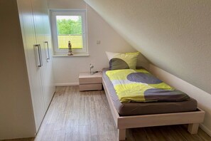 Een slaapkamer met een enkel bed, een nachtkastje, een raam en een kledingkast.