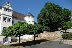 Ein Gebäude mit einem Turm, ein Baum im Vordergrund und eine Steinmauer.