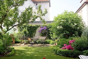 Ein Garten mit einem Holztisch und Stühlen, umgeben von üppigem Grün und blühenden Pflanzen.