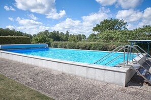 A rectangular swimming pool with a clear blue water surface, surrounded by a stone border, and a metal ladder leading into the pool. - Holiday apartment with 1 bedroom (Haffkrug)