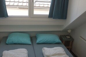 Ein Schlafzimmer mit zwei Betten, einem Fenster mit Vorhängen, einem Nachttisch mit Lampe und einem Heizkörper.