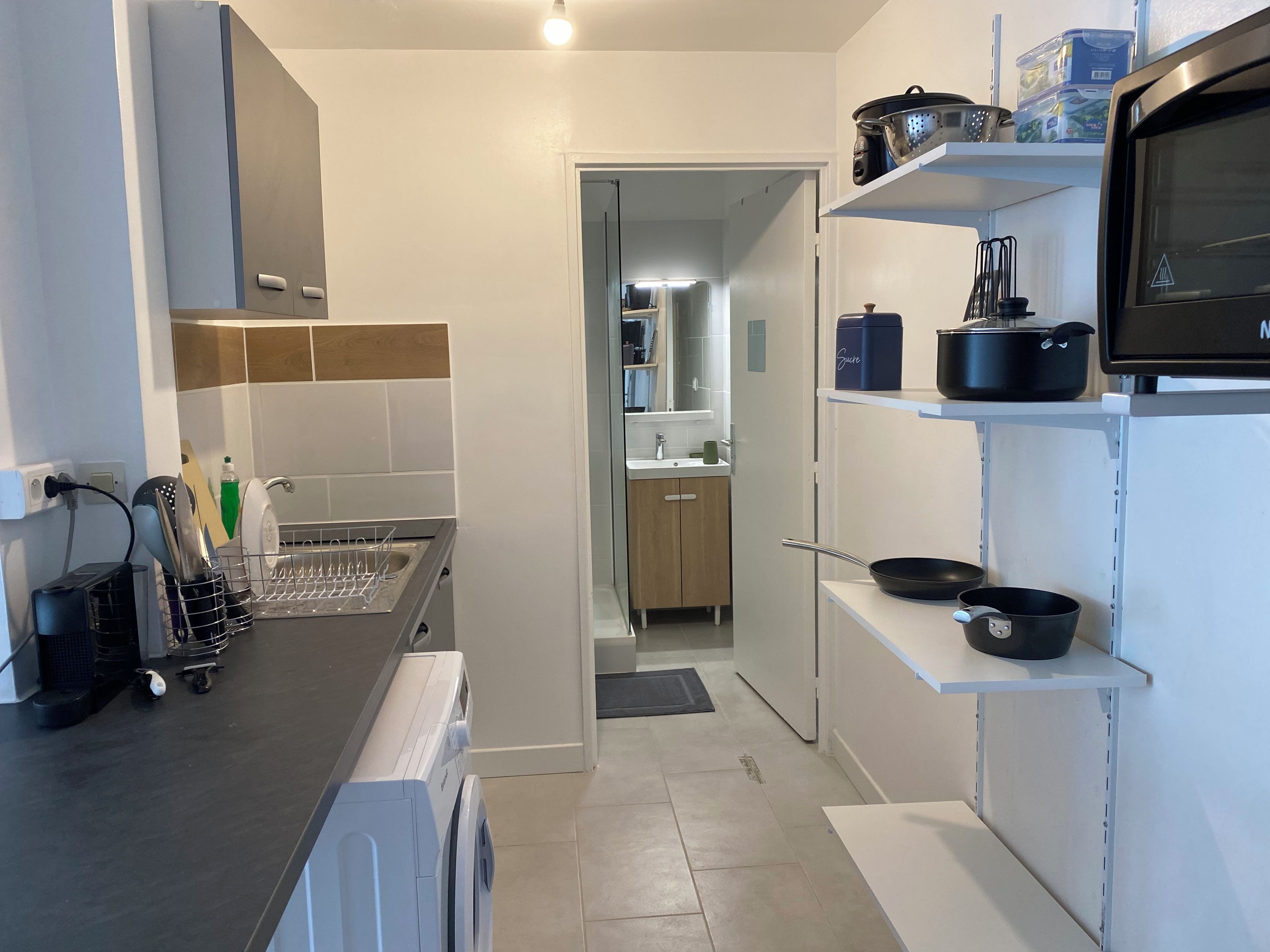 Une cuisine moderne équipée d’un lave-linge, d’un égouttoir et d’un four à micro-ondes posés sur le plan de travail.