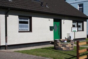 A single-story building with a green door, a small garden area with flowers, and a sign indicating a 'Frei' (free) room. - Holiday apartment with 2 bedrooms (Cuxhaven)