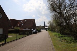 A residential street with houses, a white car parked on the side, and a tall chimney in the distance. - Holiday apartment with 1 bedroom (Borkum)