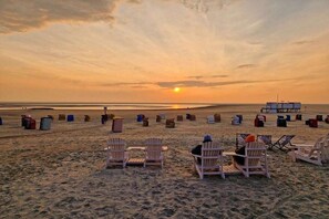 Ein Strand mit Reihen aus weißen Stühlen und Tischen, ein klarer Himmel und die Sonne, die am Horizont untergeht.